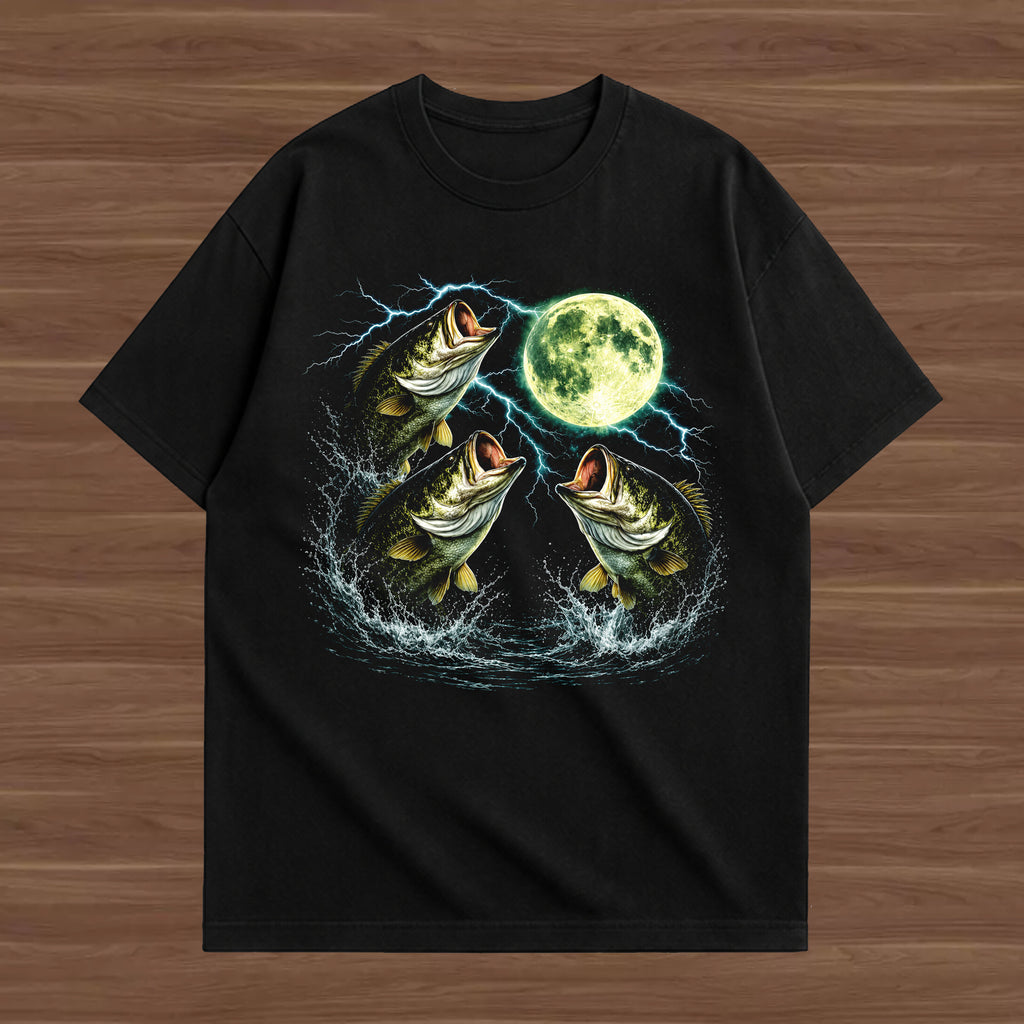 A black short-sleeve t-shirt with a graphic print of three jumping bass fish, lightning bolts, and a full moon, displayed flat on a brown wood-grain background.