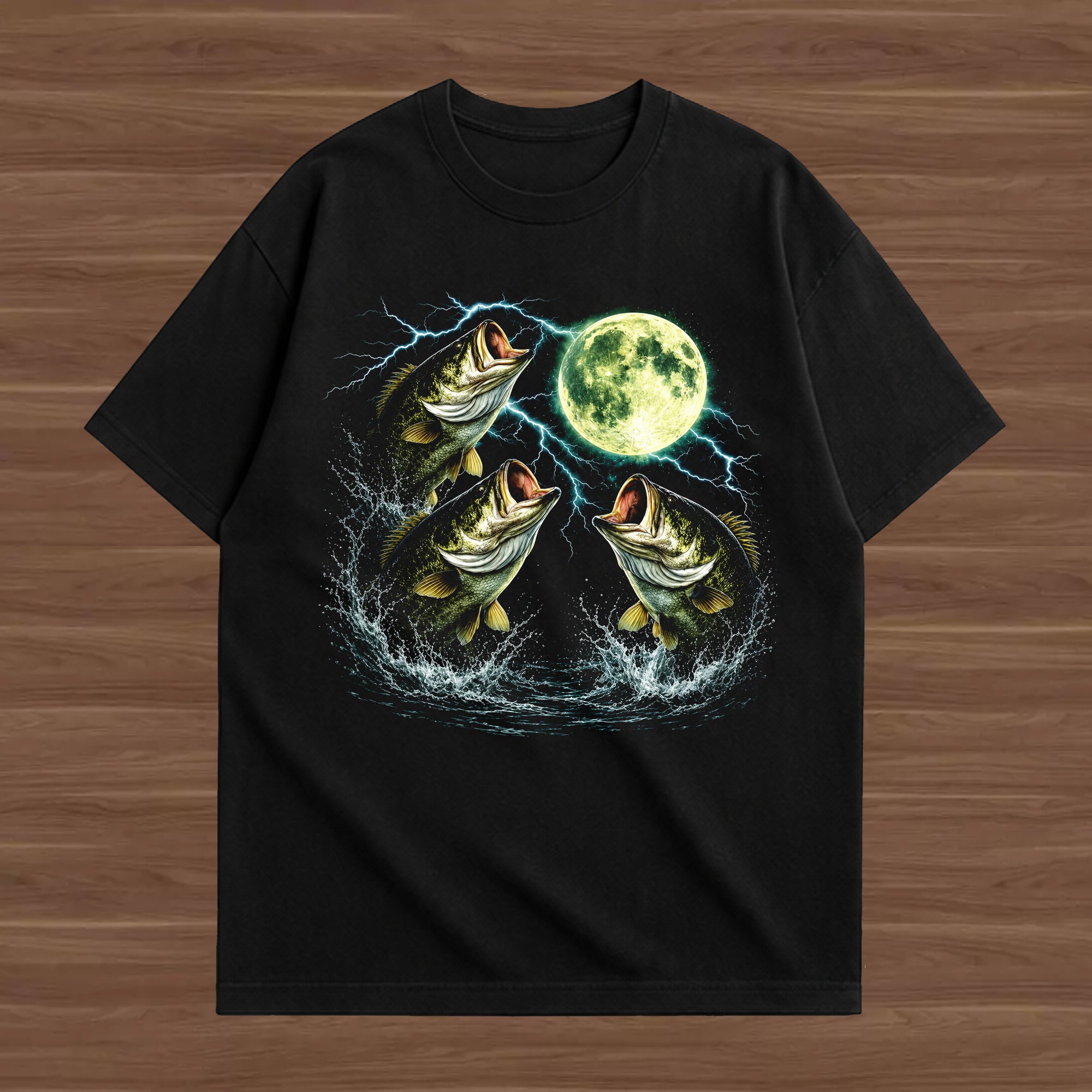 A black short-sleeve t-shirt with a graphic print of three jumping bass fish, lightning bolts, and a full moon, displayed flat on a brown wood-grain background.