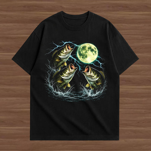 A black short-sleeve t-shirt with a graphic print of three jumping bass fish, lightning bolts, and a full moon, displayed flat on a brown wood-grain background.