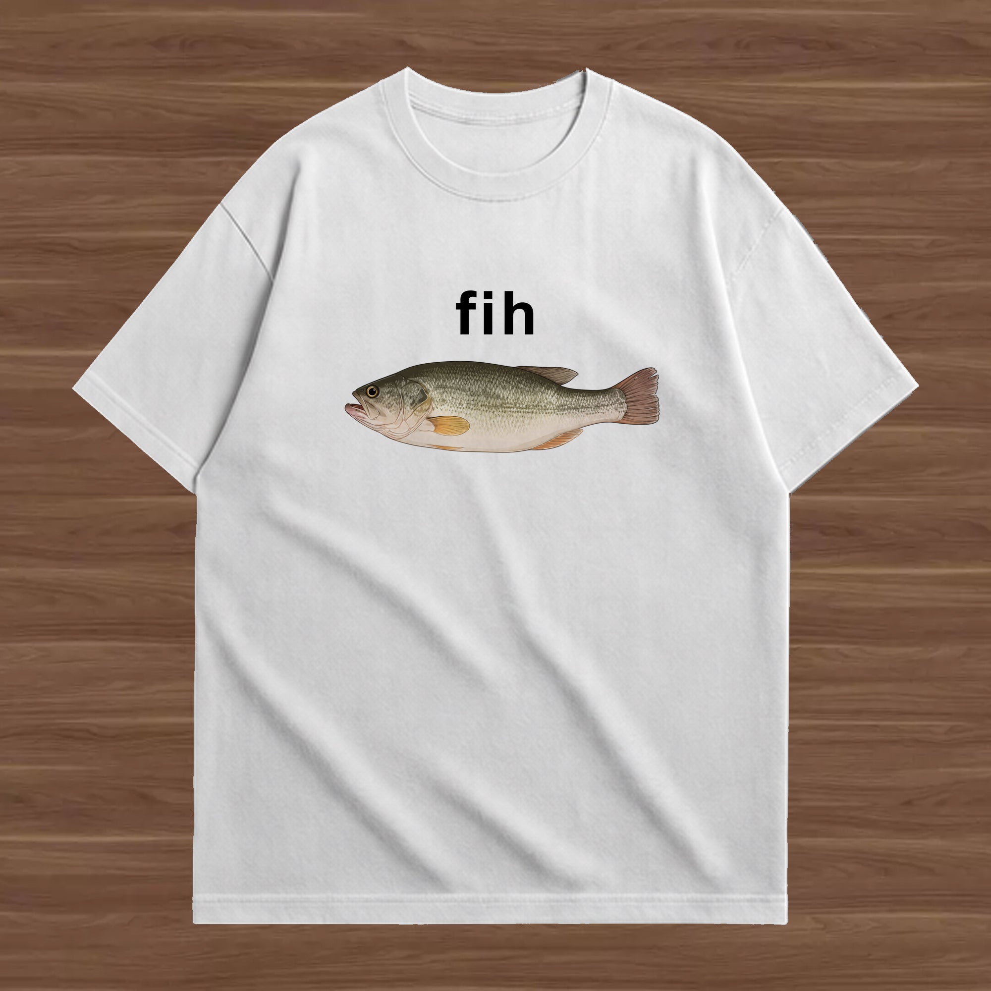 A white short-sleeve crewneck t-shirt laid flat on a brown wood-grain background. The shirt features a graphic of a largemouth bass fish with the word 'fih' printed in black above it.